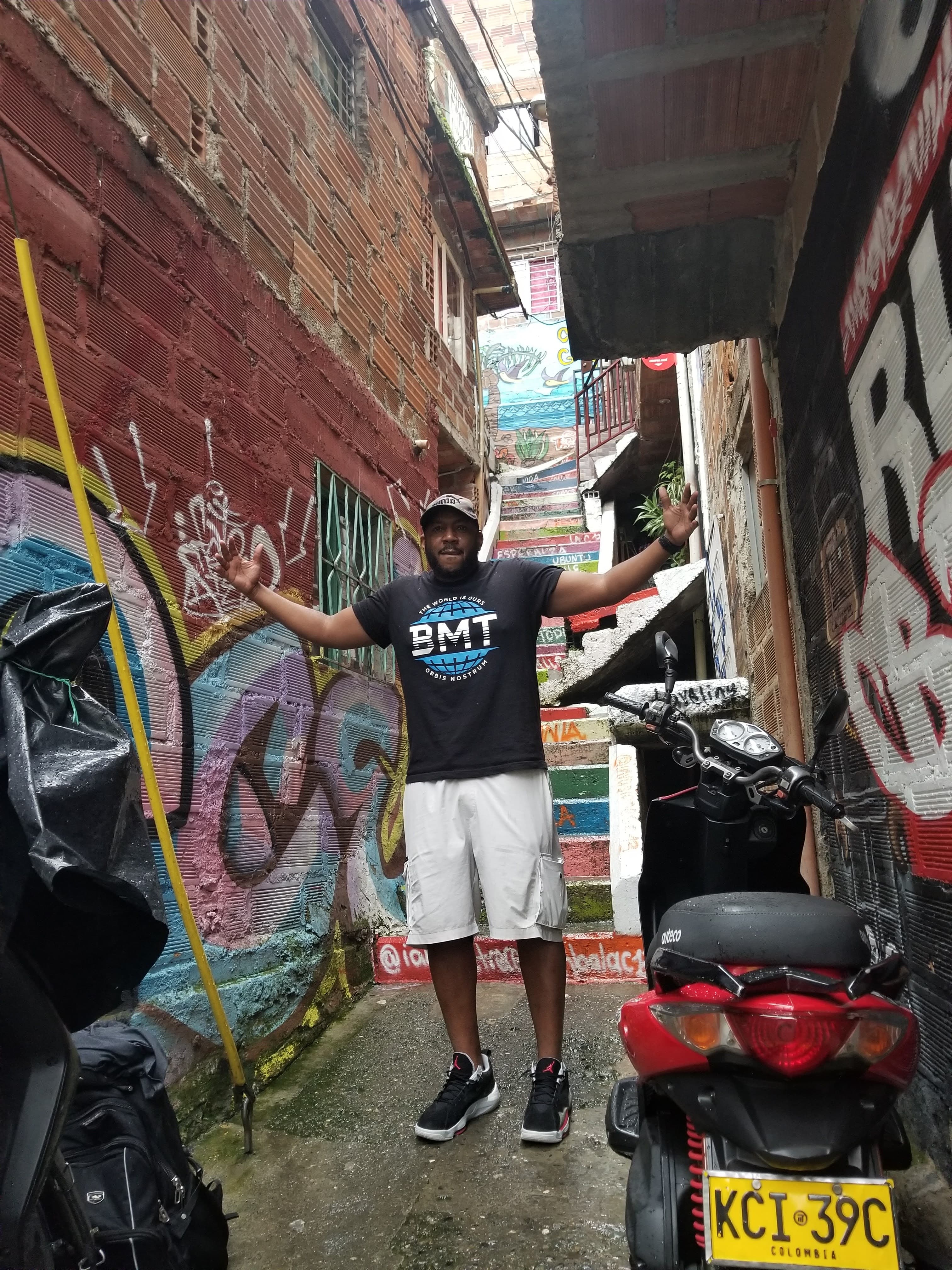Man with arms outstretched in a narrow alleyway featuring vibrant graffiti and brick buildings.