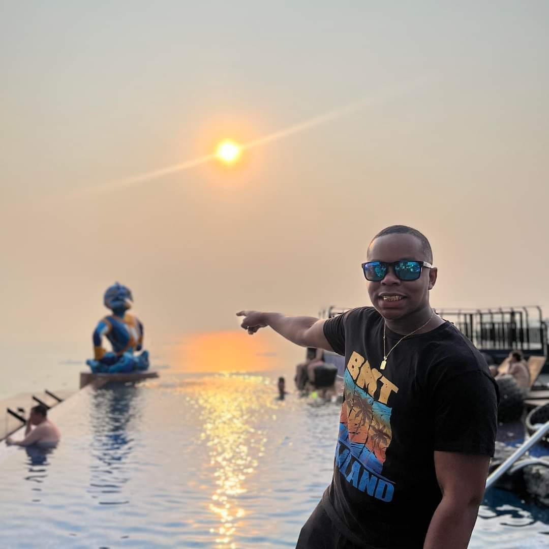Smiling man pointing at a golden sunset over an infinity pool with a blue statue.